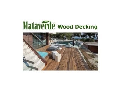  The Mataverde Wood Decking logo is displayed above an image showcasing a modern outdoor living space. A spacious FSC Machiche wood deck surrounds a pool and contemporary furniture. Glass railings and steps lead down to the area, with a building featuring wood siding in the background.